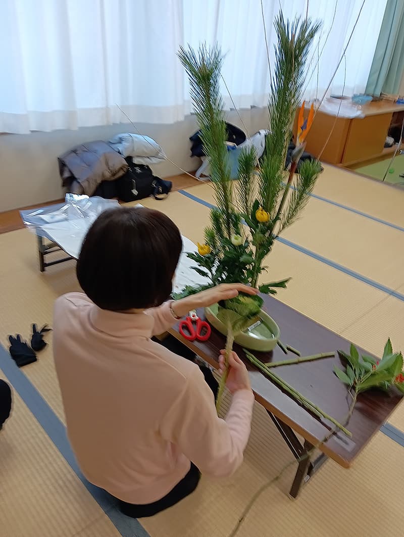 畳の上で座りながら大きな生け込みを行っている写真