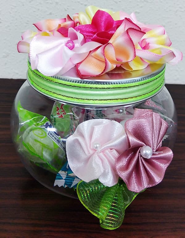 カラフルな花がフタや壺のような形をしたキャンディーボックスの横に飾られた写真です。